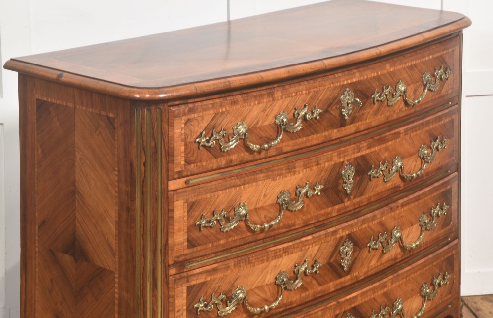 A French Louis XV style serpentine chest of drawers featuring geometric wood marquetry and decorative brass handles. View V