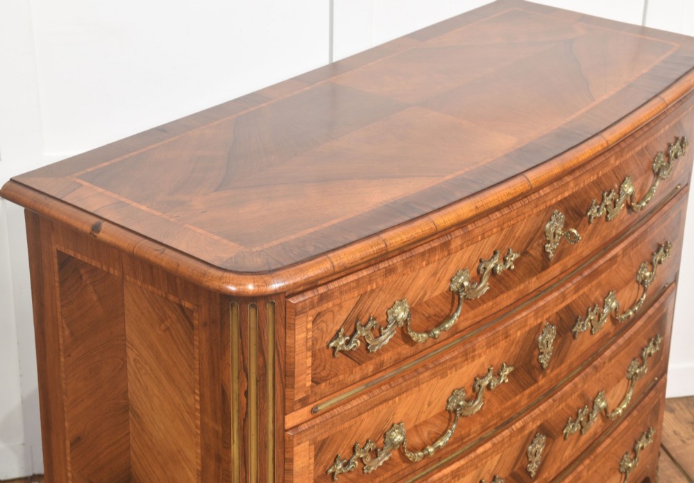 A French Louis XV style serpentine chest of drawers featuring geometric wood marquetry and decorative brass handles. View VI