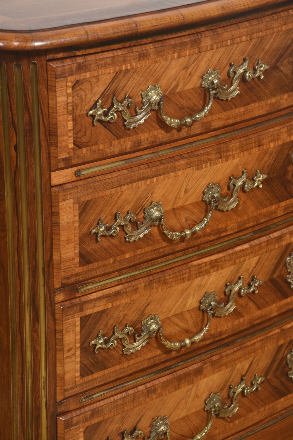 A French Louis XV style serpentine chest of drawers featuring geometric wood marquetry and decorative brass handles. View VII