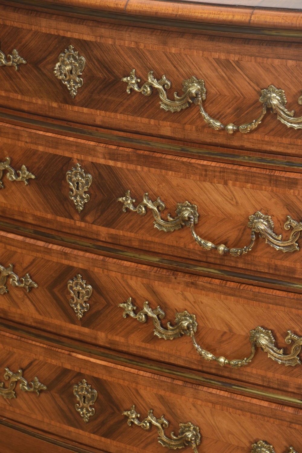 A French Louis XV style serpentine chest of drawers featuring geometric wood marquetry and decorative brass handles. View VIII
