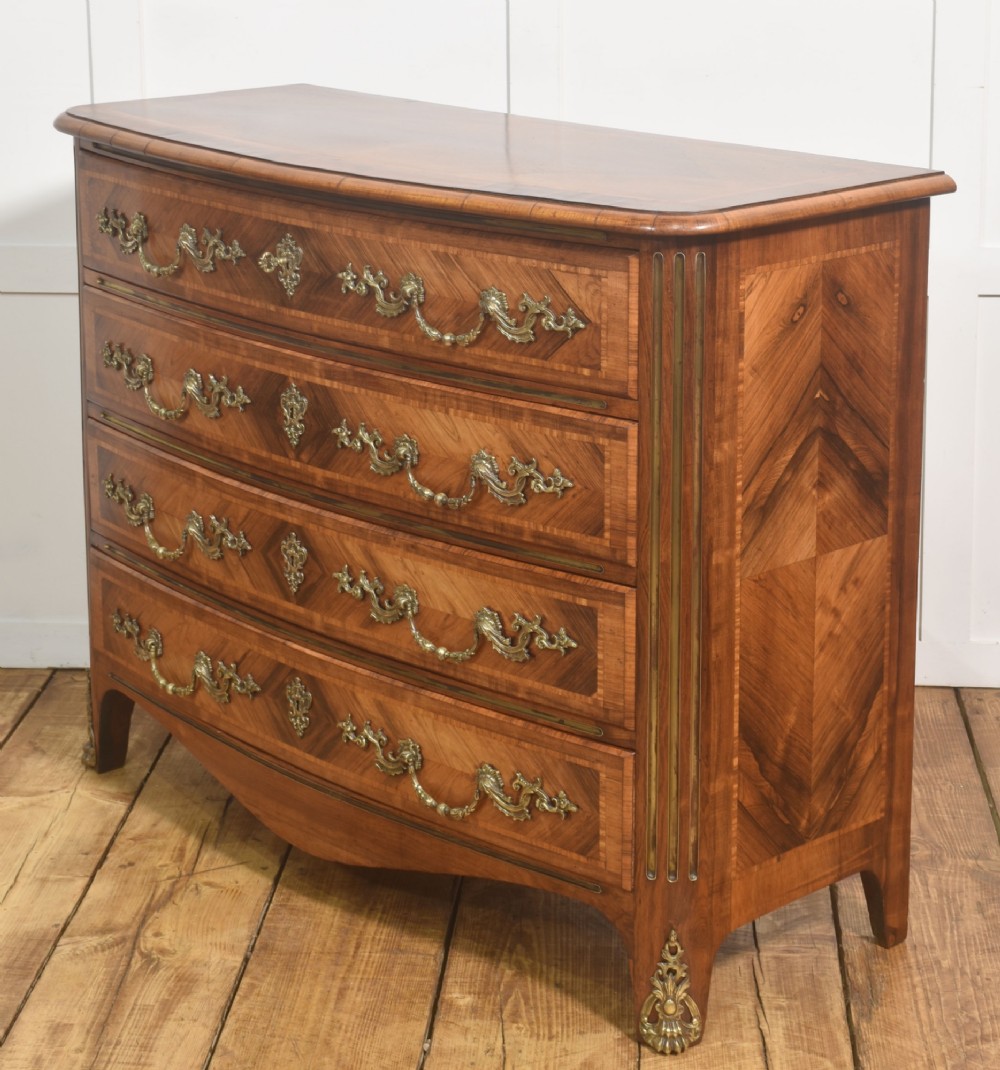 A French Louis XV style serpentine chest of drawers featuring geometric wood marquetry and decorative brass handles. View IX