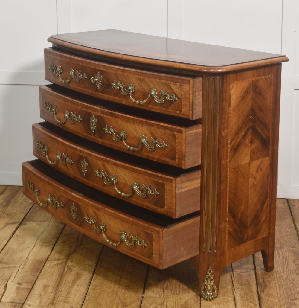 A French Louis XV style serpentine chest of drawers featuring geometric wood marquetry and decorative brass handles. View XI