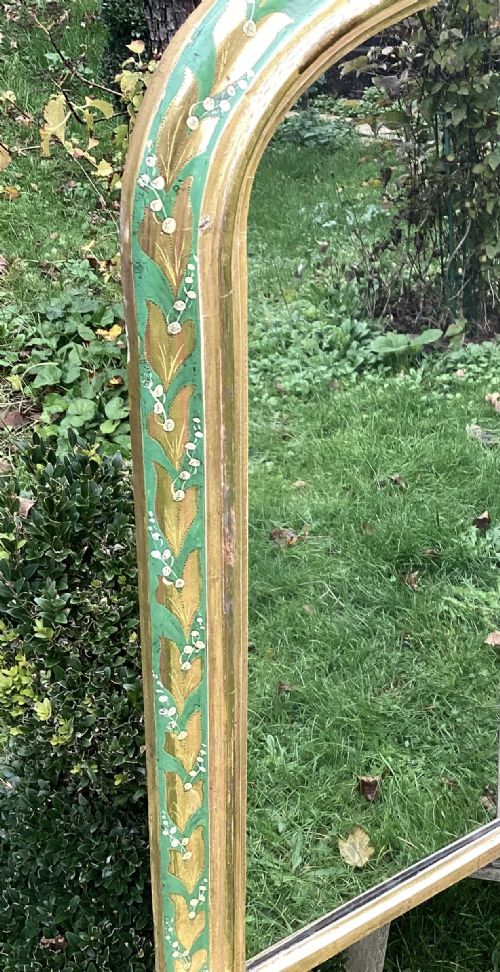 fig 1. An arched Victorian giltwood overmantel mirror featuring hand-painted lily of the valley floral motifs along the upper frame and white ceramic feet.