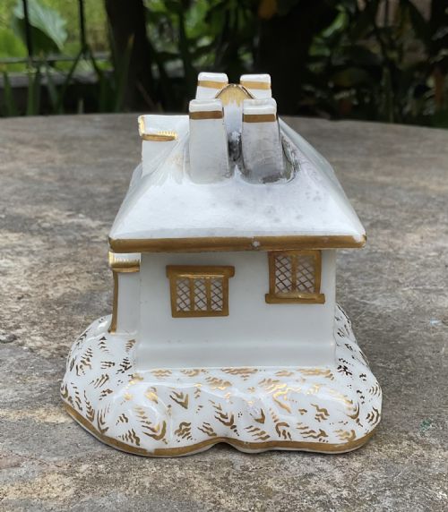 fig 1. A Regency period white porcelain pastille burner shaped as a cottage featuring gilded chimneys, dormer window, and lattice pattern windows.