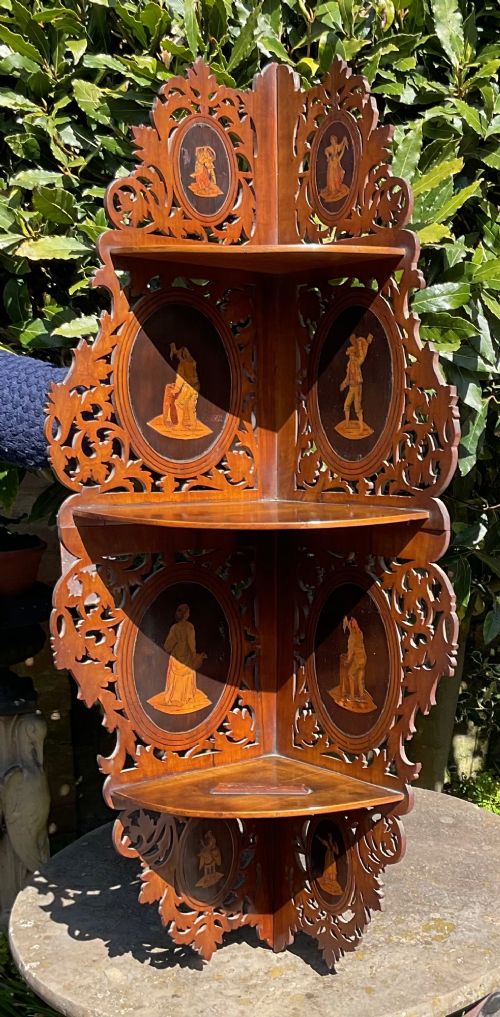 A Victorian three-tiered olive wood corner shelf with pierced fretwork edges and oval inlaid marquetry panels depicting Italian figures. View V