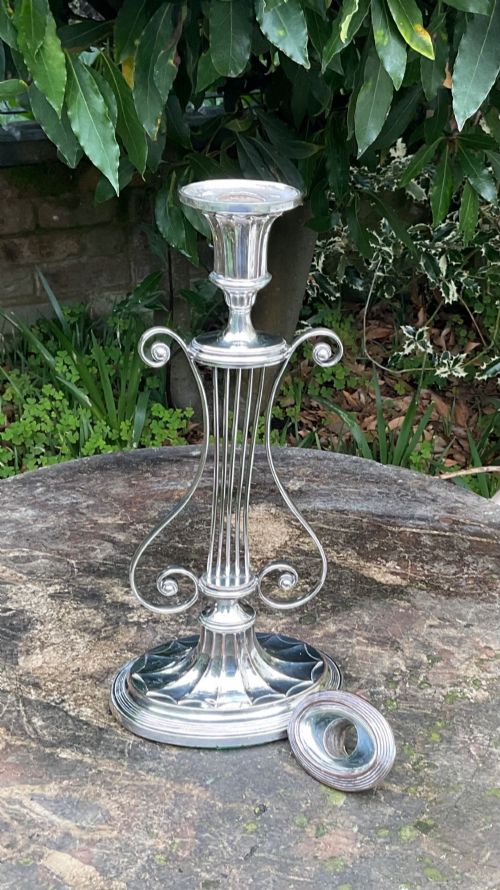 fig 1. A tall silver-plated candlestick designed in the Adam style featuring a lyre-shaped central column, scroll motifs, and a fluted sconce over a circular moulded base.