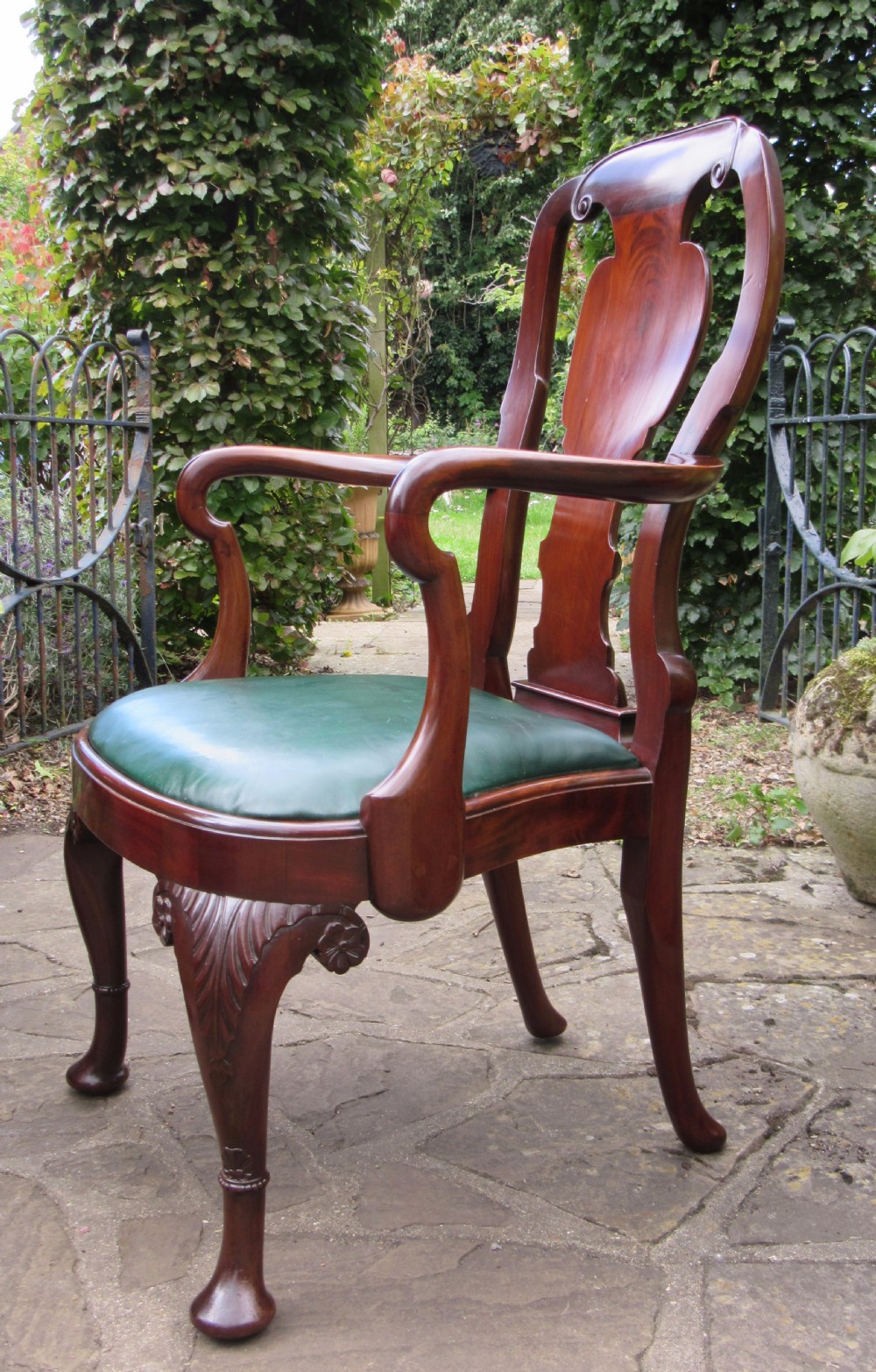A Georgian style dark mahogany open armchair featuring a vase-shaped back splat, curved arms, a green leather seat, and carved cabriole front legs. View II