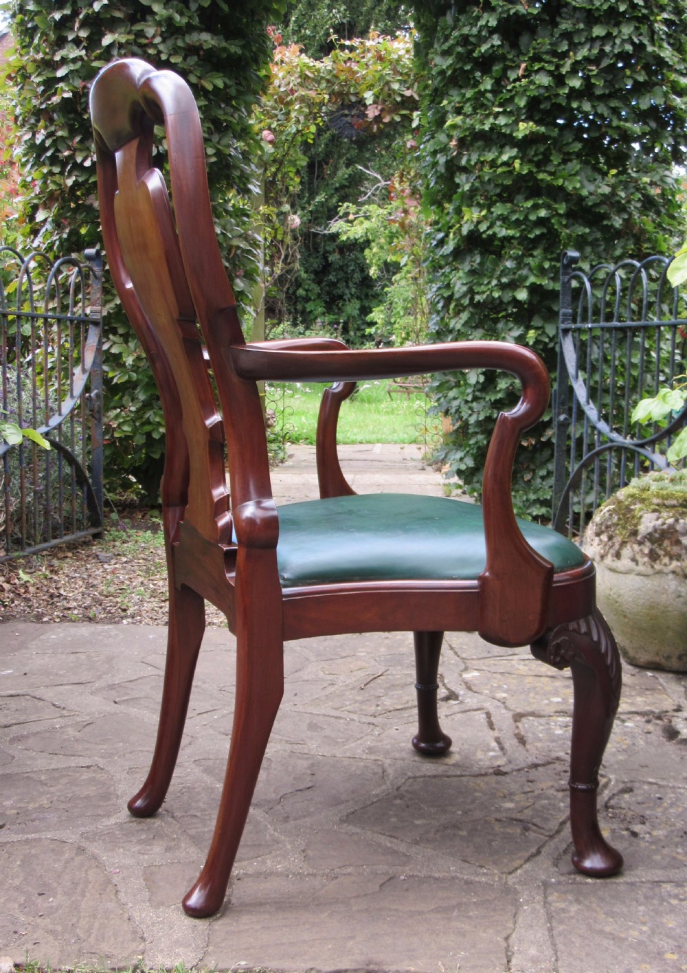 A Georgian style dark mahogany open armchair featuring a vase-shaped back splat, curved arms, a green leather seat, and carved cabriole front legs. View IV