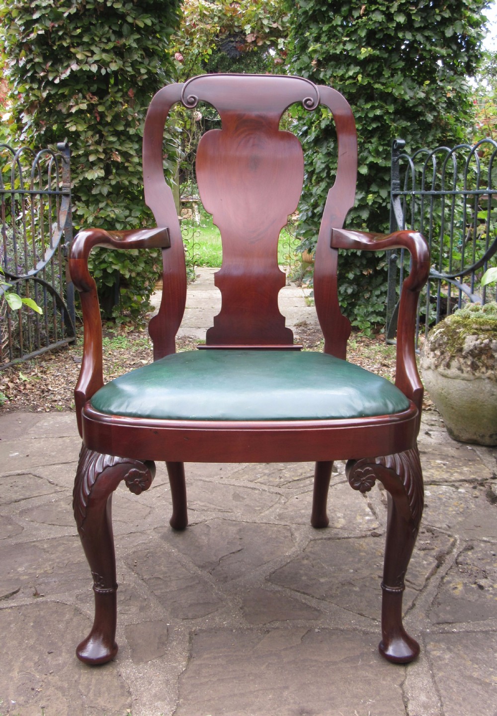 A Georgian style dark mahogany open armchair featuring a vase-shaped back splat, curved arms, a green leather seat, and carved cabriole front legs. View IX
