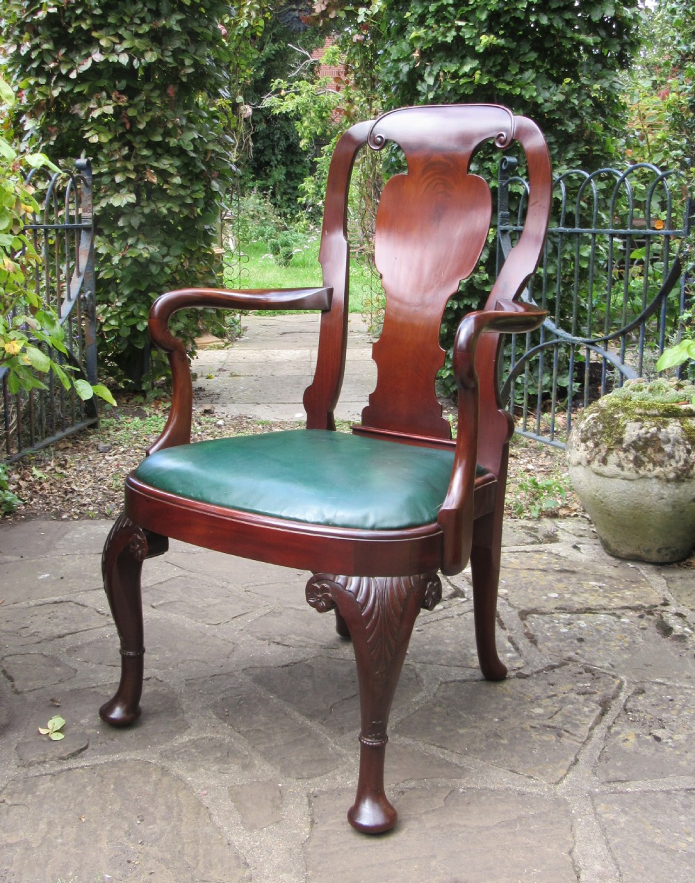 A Georgian style dark mahogany open armchair featuring a vase-shaped back splat, curved arms, a green leather seat, and carved cabriole front legs. View X