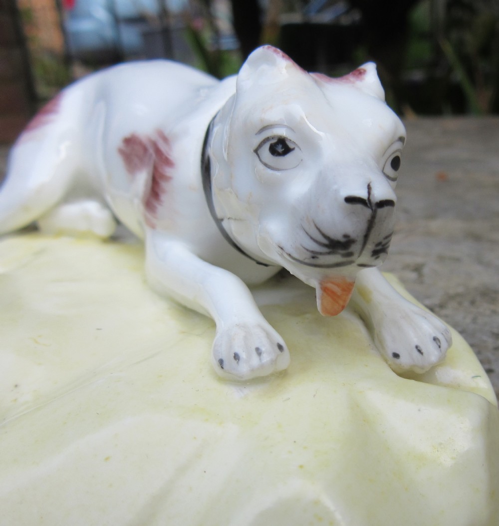 An antique Victorian white porcelain figurine of a reclining mastiff dog with reddish patches on a pale yellow gilded base. View IV