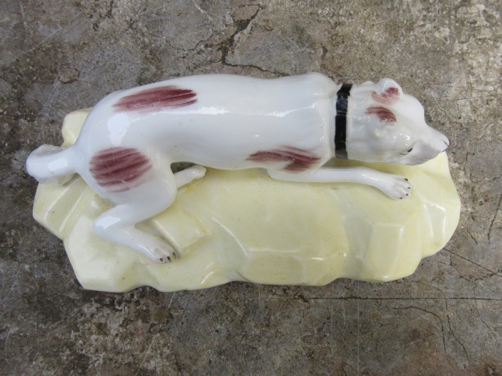 An antique Victorian white porcelain figurine of a reclining mastiff dog with reddish patches on a pale yellow gilded base. View V