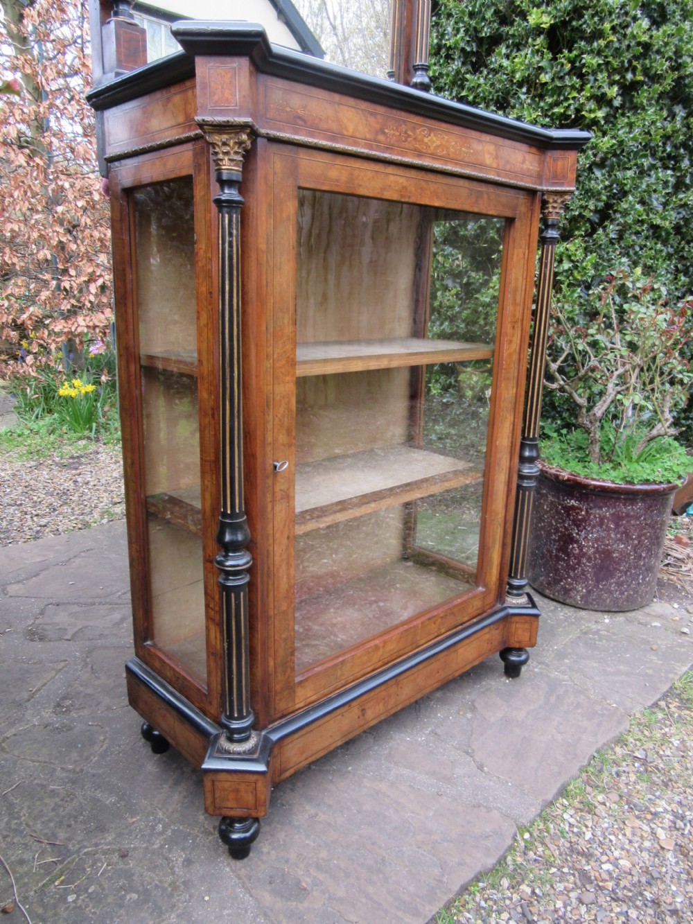 A Victorian walnut display cabinet with a single glazed door, side glass panels, floral marquetry, ebonised columns, and an upper mirror frame topped with finials. View IV