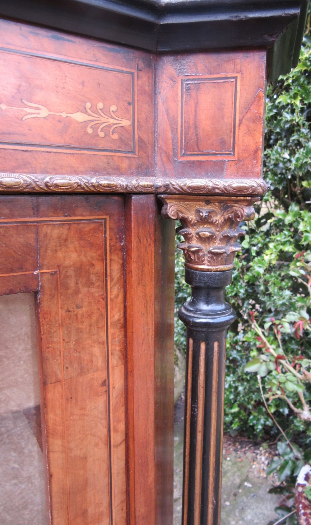 A Victorian walnut display cabinet with a single glazed door, side glass panels, floral marquetry, ebonised columns, and an upper mirror frame topped with finials. View VI