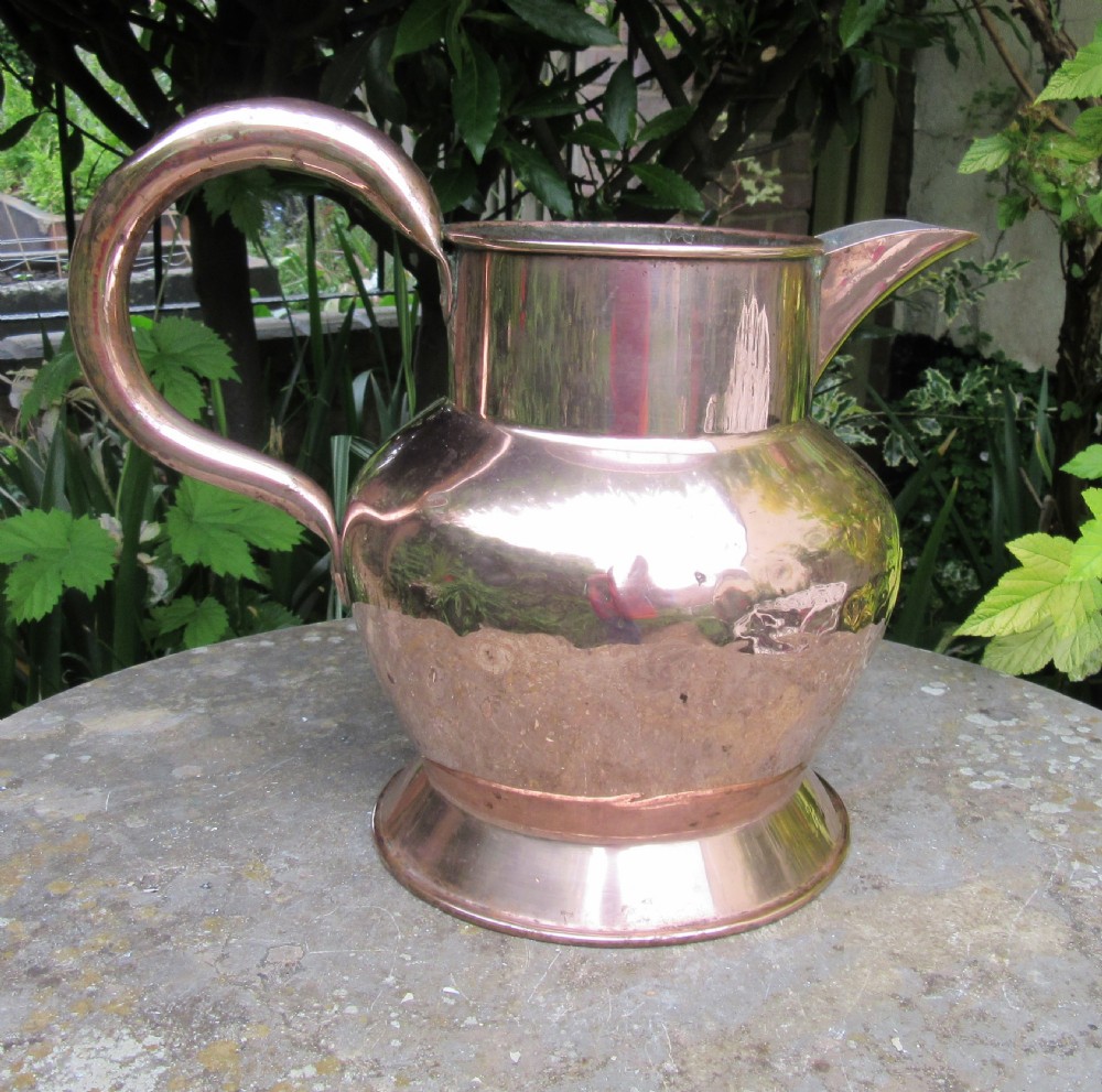 A polished Georgian copper tavern jug featuring a bulbous body, cylindrical neck, pouring spout, flared base, and a thick curved handle.