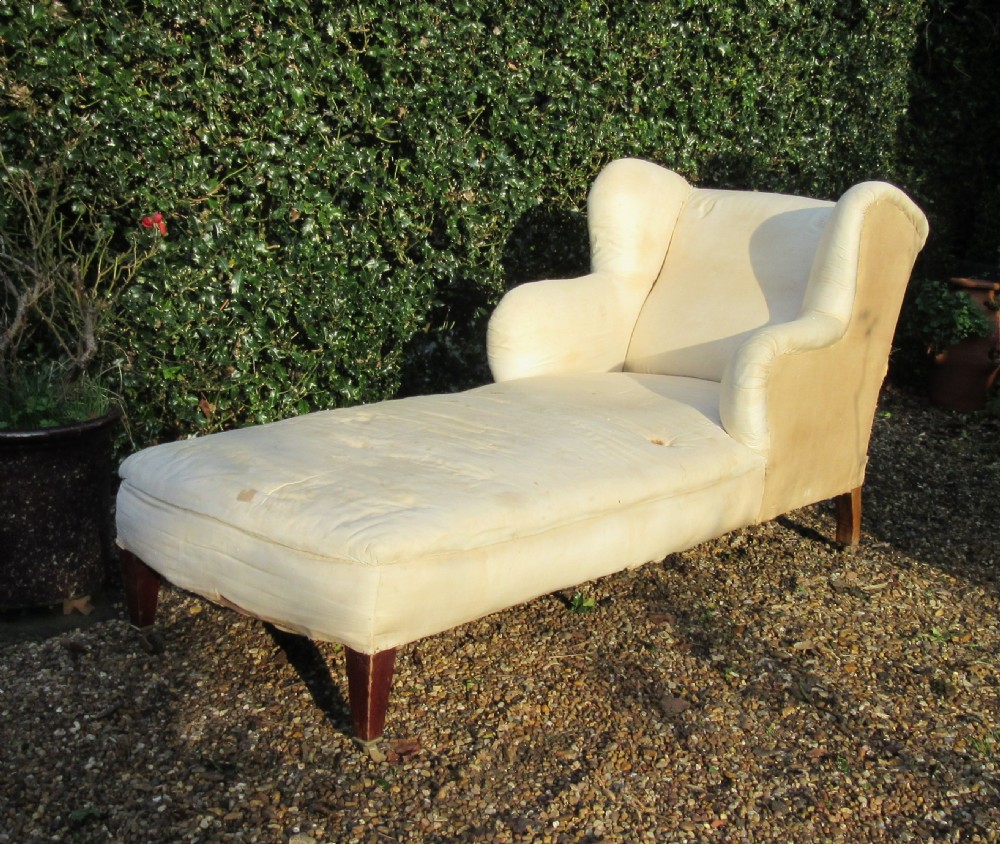 An antique cream calico upholstered day bed featuring a high wingback headrest, tapered mahogany legs, and brass castors.