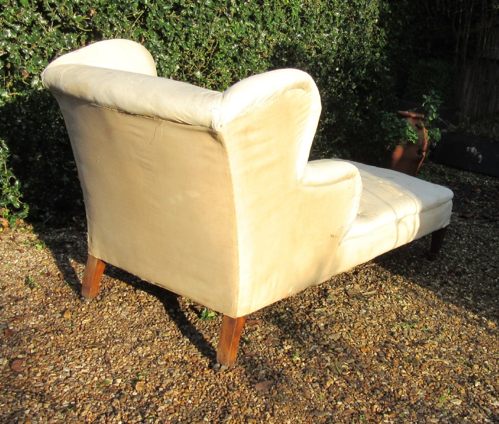 An antique cream calico upholstered day bed featuring a high wingback headrest, tapered mahogany legs, and brass castors. View IV