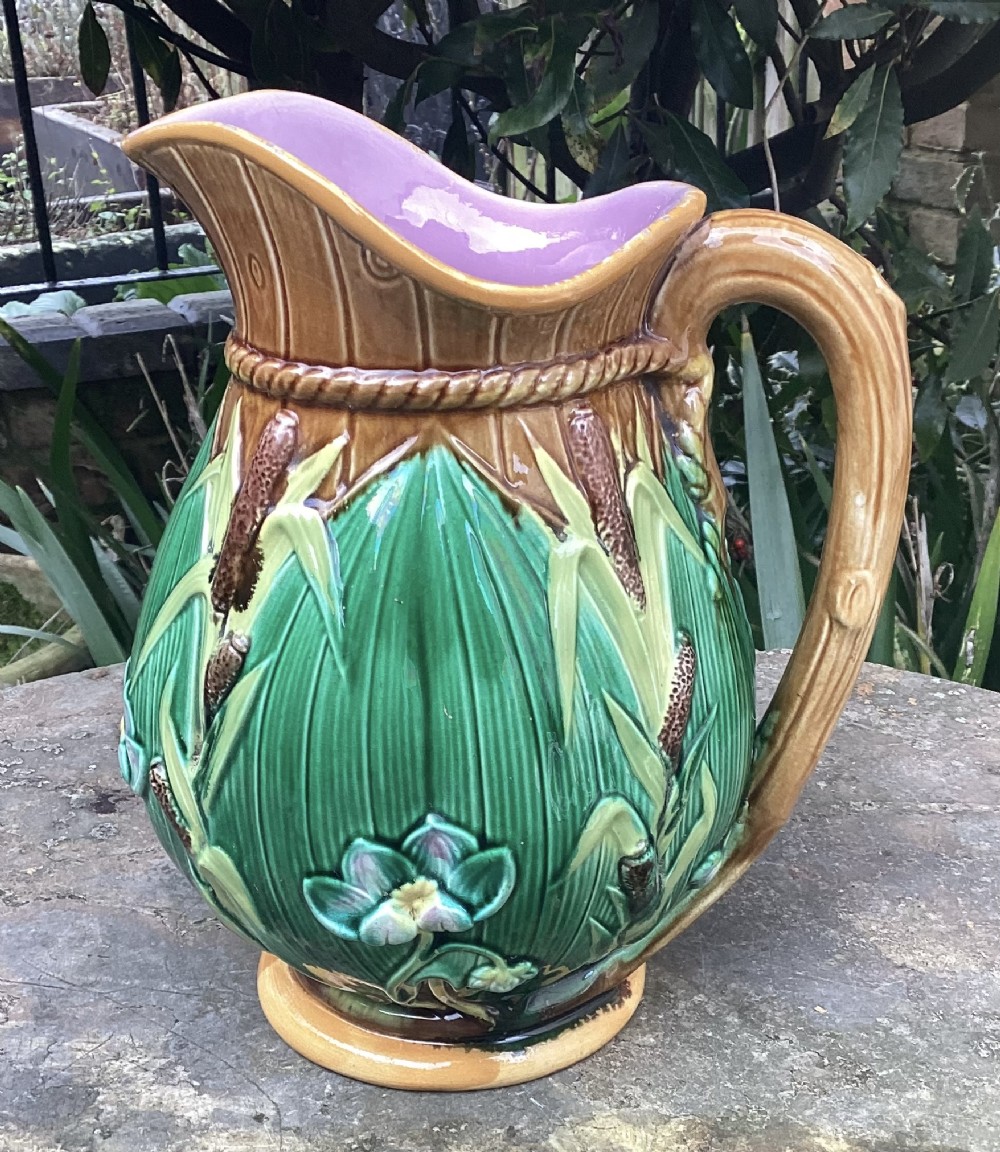 An antique Victorian George Jones majolica jug with relief-moulded green leaves, brown bulrushes, a water lily motif, and a pink glazed interior.