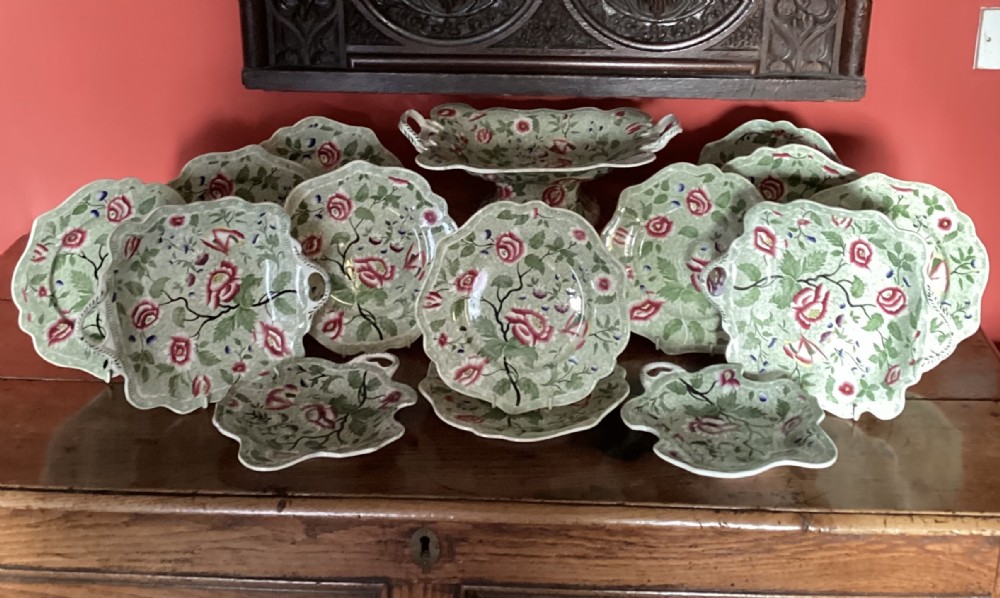 An English Regency ceramic dessert service decorated with a dense green leafy pattern and pink floral motifs, featuring plates, leaf dishes, and a footed compote.