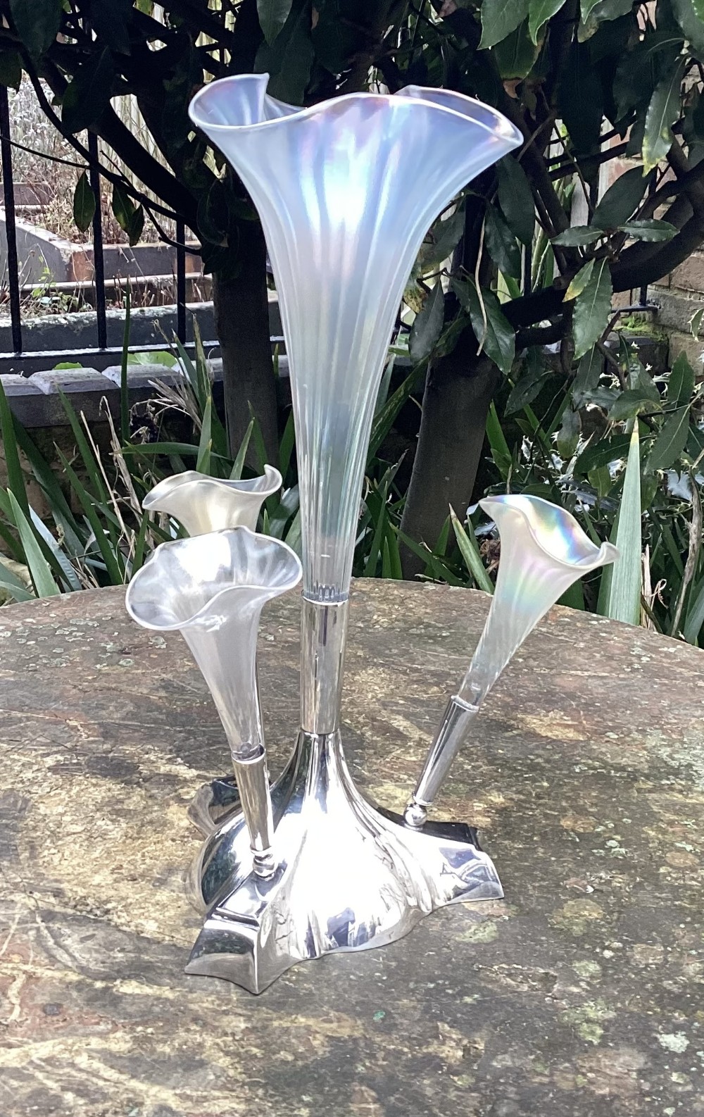 An Edwardian silver-plated epergne featuring a central tall trumpet vase flanked by three smaller trumpet-shaped branches made from pearlescent iridescent glass.