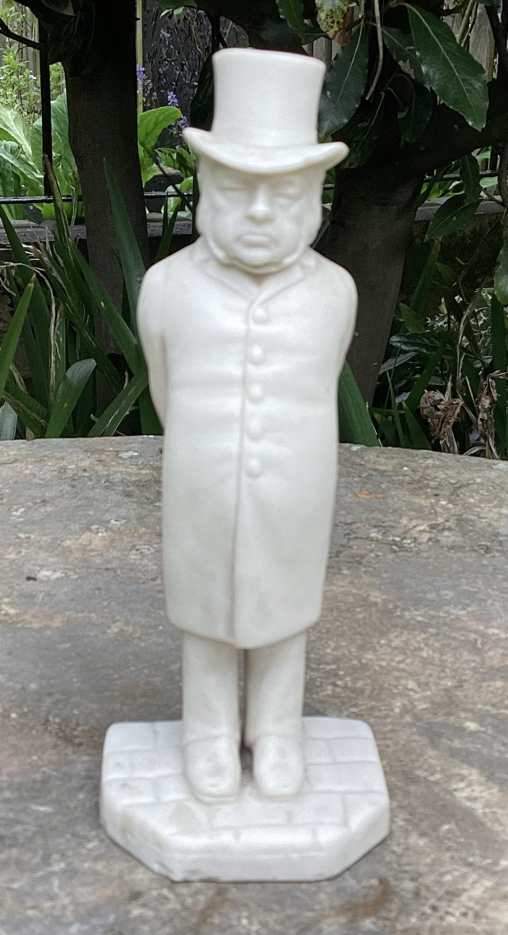 An off-white Victorian parian porcelain figurine of a gentleman wearing a top hat and buttoned frock coat standing on a cobblestone base.