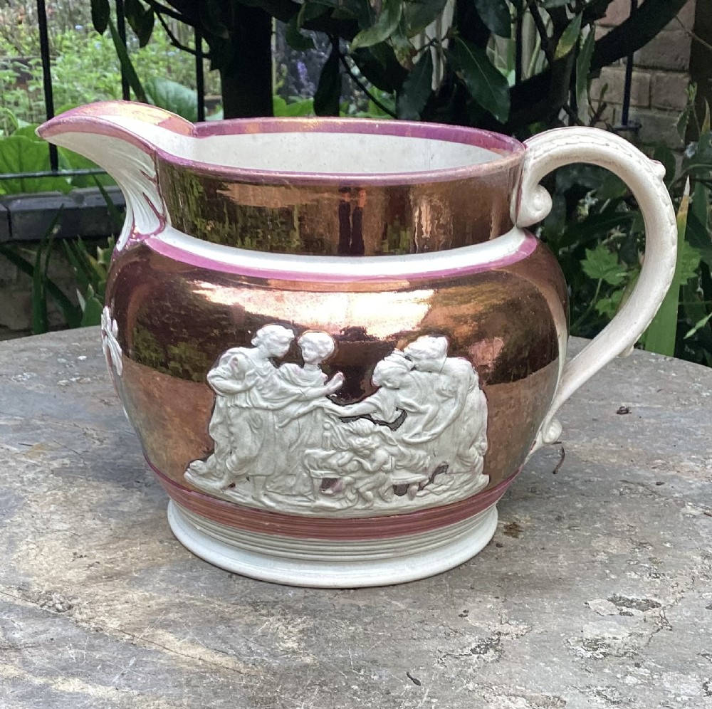 A Georgian era ceramic copper lustre jug decorated with white classical figures in relief around the body.