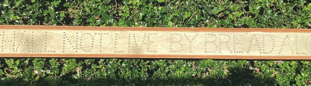 A long horizontal painted pine sign with metal stud lettering spelling out MAN SHALL NOT LIVE BY BREAD ALONE. View V