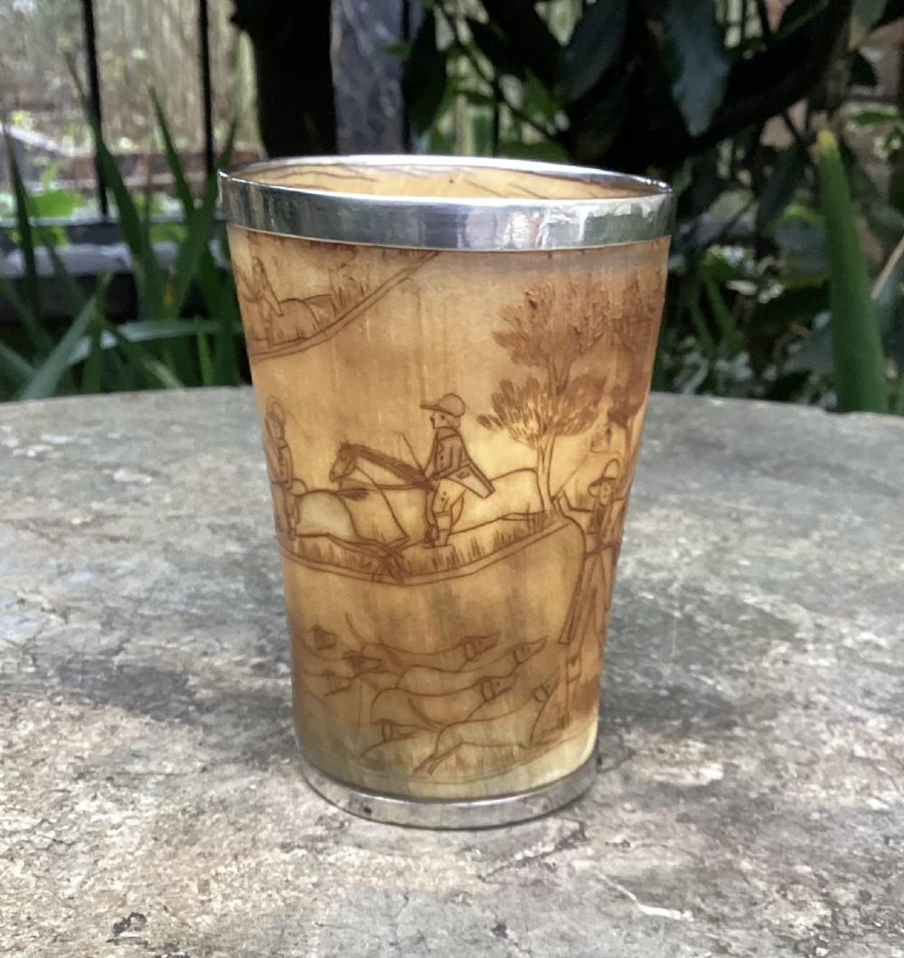 A tapered translucent horn beaker featuring hand-engraved fox hunting scenes and silver mounts along the top rim and base.