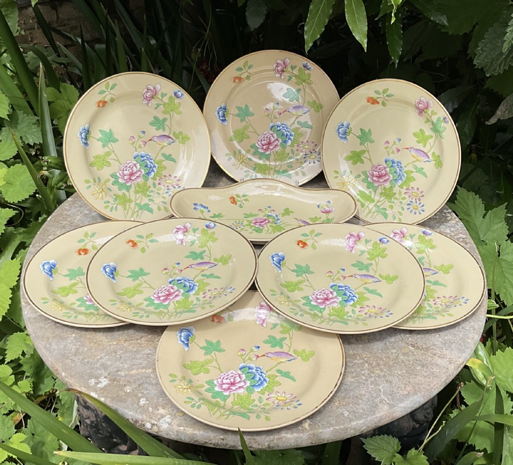 An antique Wedgwood drabware dessert service featuring several round plates and an elongated serving dish decorated with hand-painted botanical flowers and birds.