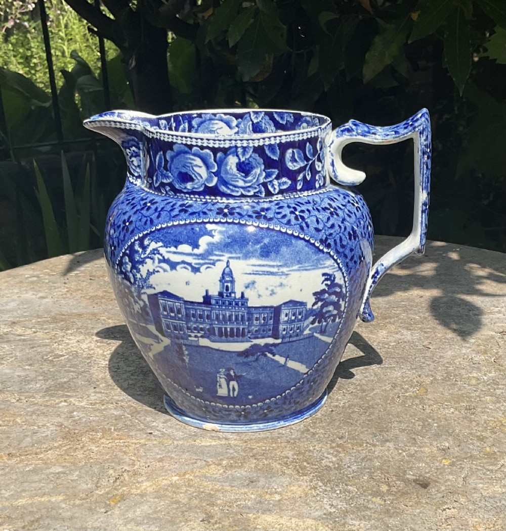A Georgian blue and white ceramic jug featuring an underglaze transfer print depicting an architectural building surrounded by a floral border.