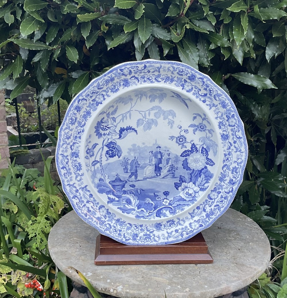 A large Victorian blue and white stone china charger featuring a Chinoiserie landscape scene with figures and an intricate floral border.