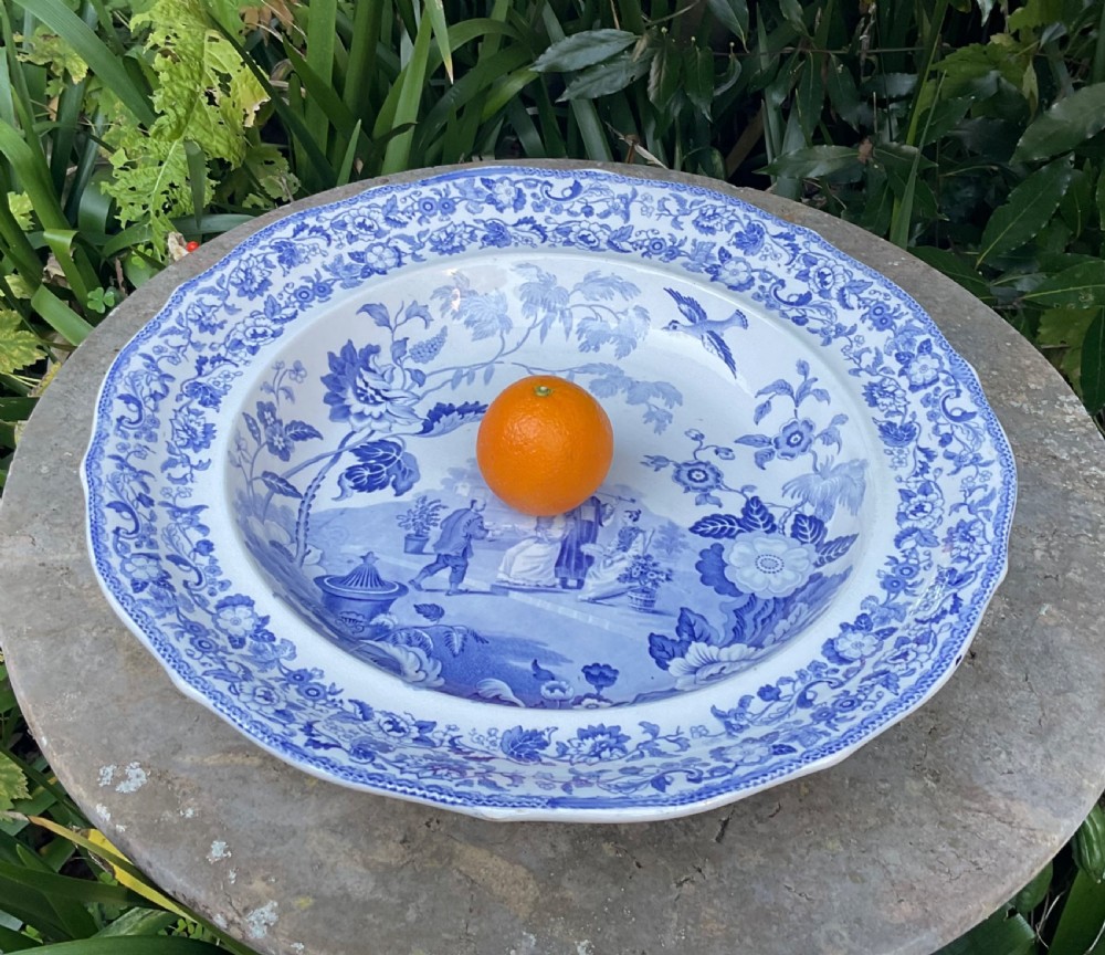 A large Victorian blue and white stone china charger featuring a Chinoiserie landscape scene with figures and an intricate floral border. View VI