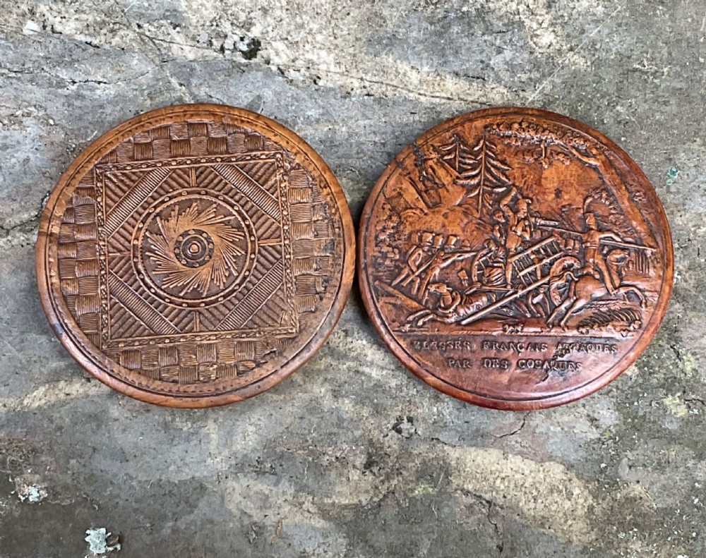 A circular antique pressed maple wooden snuff box lid featuring a raised relief scene of a military battle scene with horses and soldiers. View IV