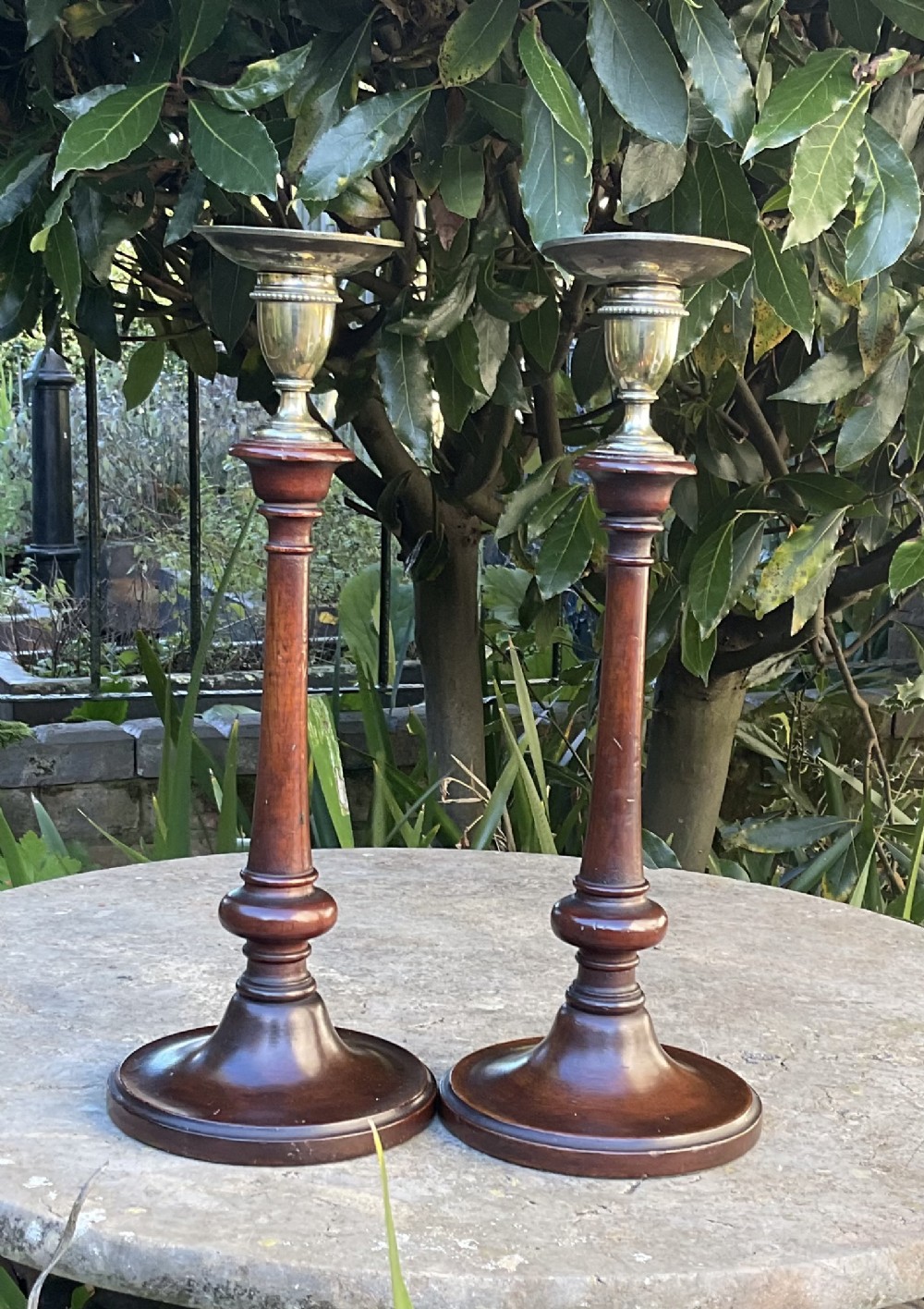 A pair of late Victorian turned mahogany candlesticks featuring stepped circular bases and brass sconces.