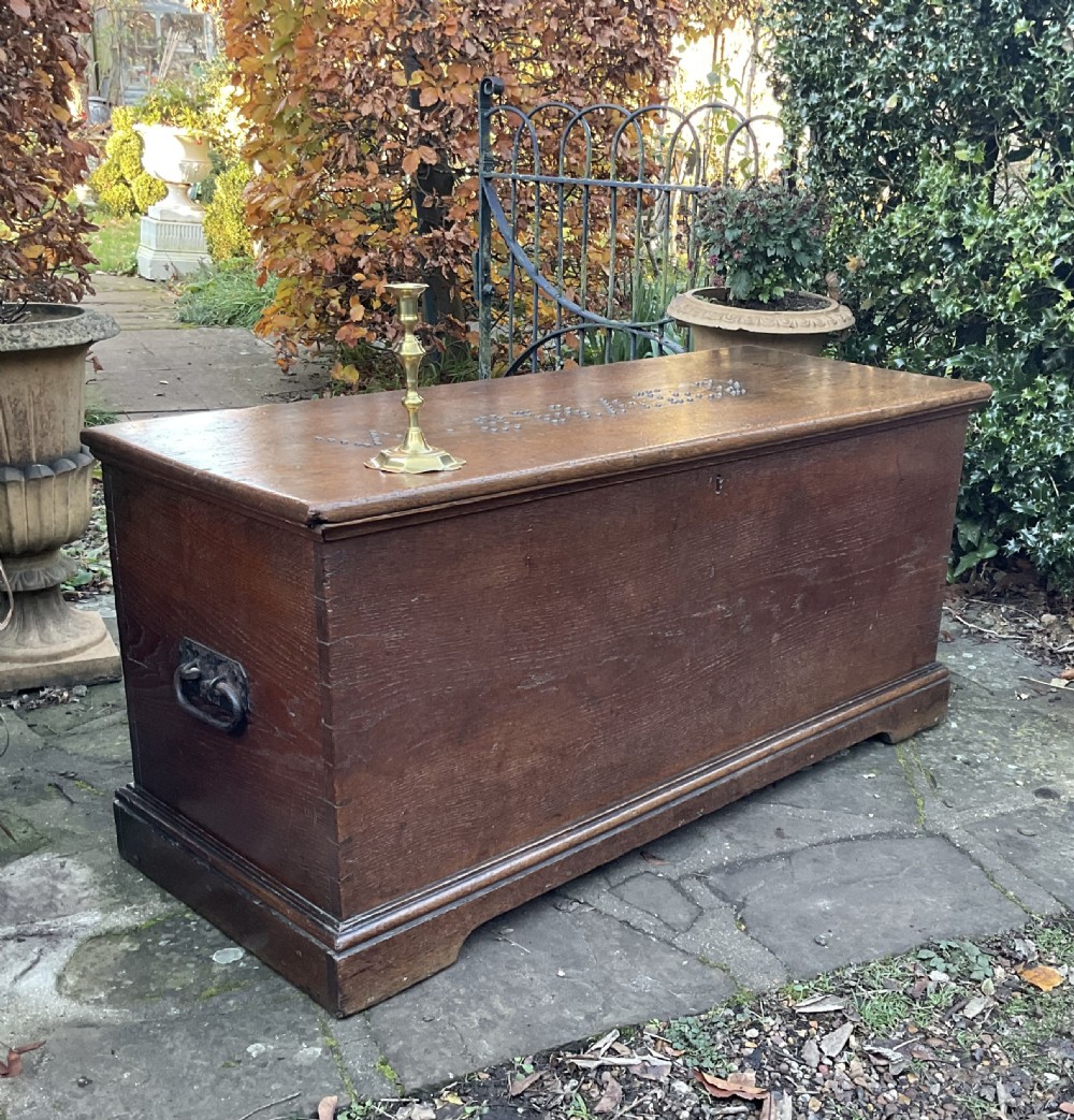 A rectangular Georgian dark oak blanket box featuring brass studding on the lid, wrought iron side handles, and a moulded plinth base.