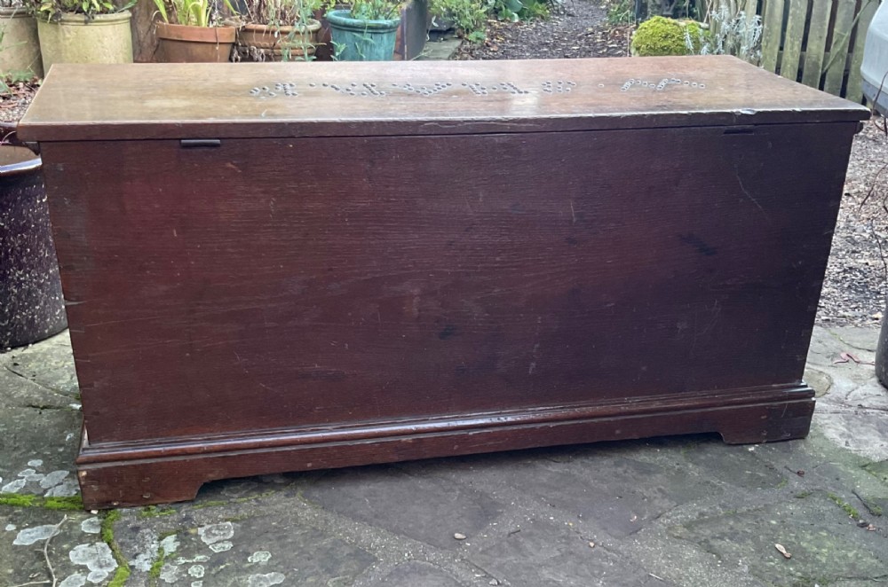A rectangular Georgian dark oak blanket box featuring brass studding on the lid, wrought iron side handles, and a moulded plinth base. View IV