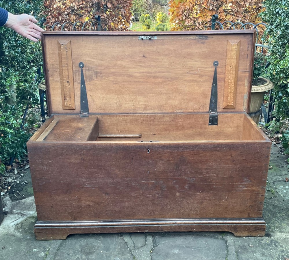 A rectangular Georgian dark oak blanket box featuring brass studding on the lid, wrought iron side handles, and a moulded plinth base. View V