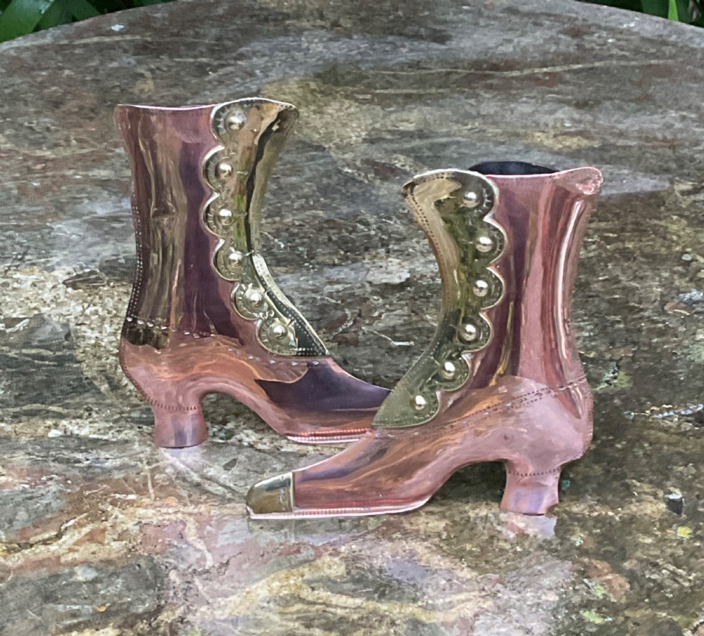 A pair of polished copper boot ornaments featuring scalloped brass button trims and brass toe caps facing each other. View IV