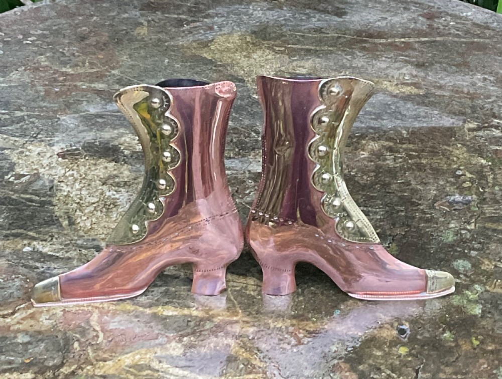 A pair of polished copper boot ornaments featuring scalloped brass button trims and brass toe caps facing each other. View V