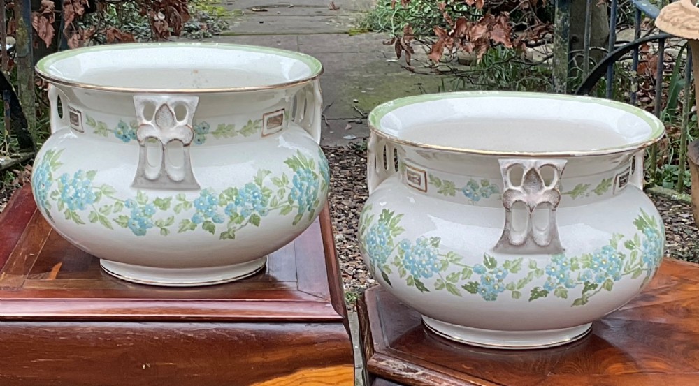 A pair of cream English pottery jardinieres featuring blue floral garlands, gilded rims, and three reticulated handles.
