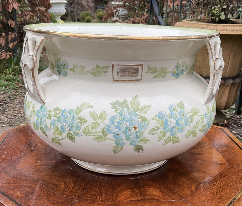 A pair of cream English pottery jardinieres featuring blue floral garlands, gilded rims, and three reticulated handles. View V