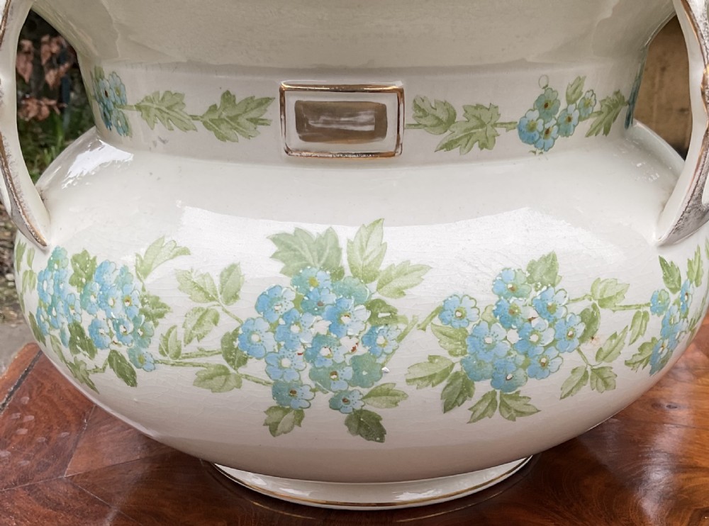 A pair of cream English pottery jardinieres featuring blue floral garlands, gilded rims, and three reticulated handles. View VII