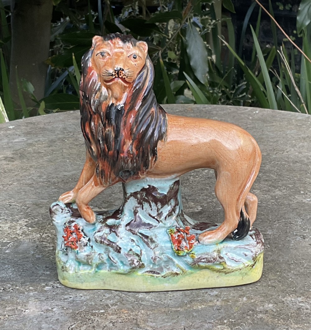 A Victorian Staffordshire earthenware figurine depicting a tawny brown lion standing on a rocky turquoise base.