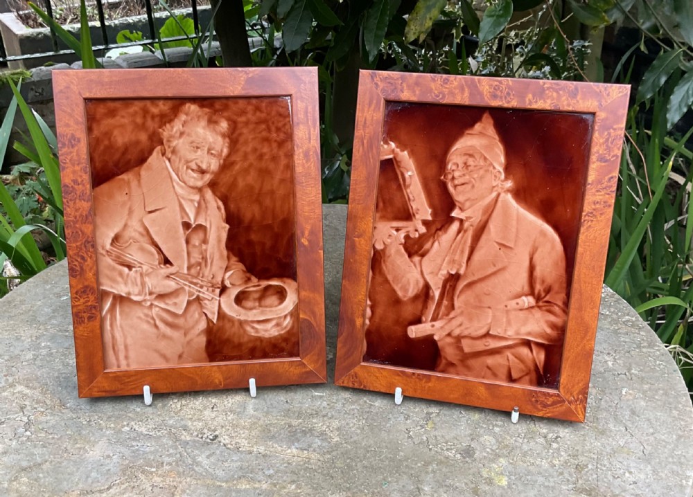 A pair of framed, warm brown glaze ceramic tiles depicting musician figures in sepia relief.