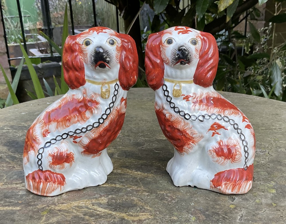 A pair of Victorian earthenware Staffordshire spaniel figurines painted with red patches, black snouts, and gilt chains.