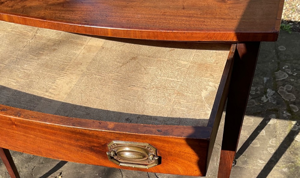 A Georgian mahogany bow-front side table featuring a single drawer with brass handles and slender tapered legs on brass castors. View VIII
