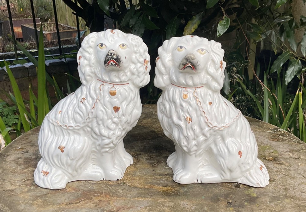 A pair of Victorian white glazed earthenware Staffordshire spaniel dog figurines with gilded accents and hand-painted facial features.