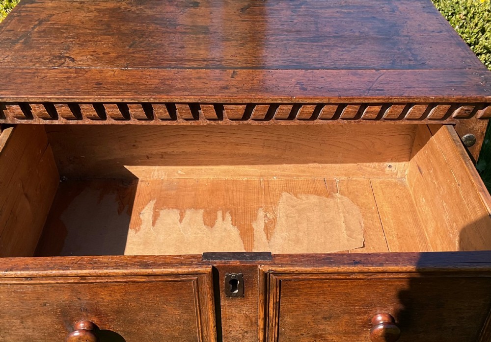 A 17th-century English dark oak chest of drawers featuring geometric panel mouldings, turned wooden knobs, split-spindle side mouldings, and a scalloped base. View IX