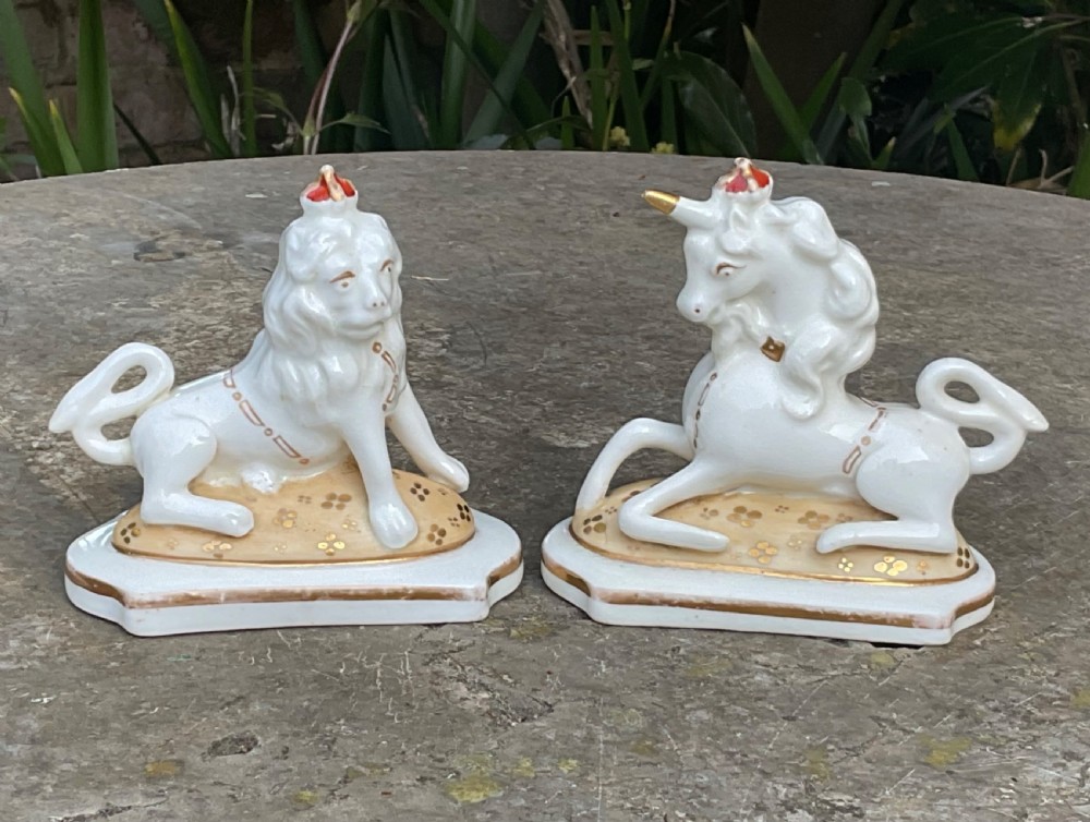 A pair of Victorian Staffordshire white glazed ceramic figures depicting a recumbent royal lion and unicorn with gilded detailing on moulded bases.
