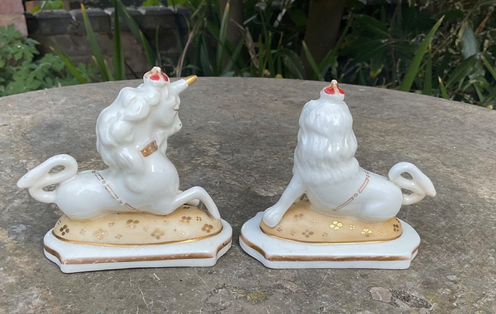 A pair of Victorian Staffordshire white glazed ceramic figures depicting a recumbent royal lion and unicorn with gilded detailing on moulded bases. View II